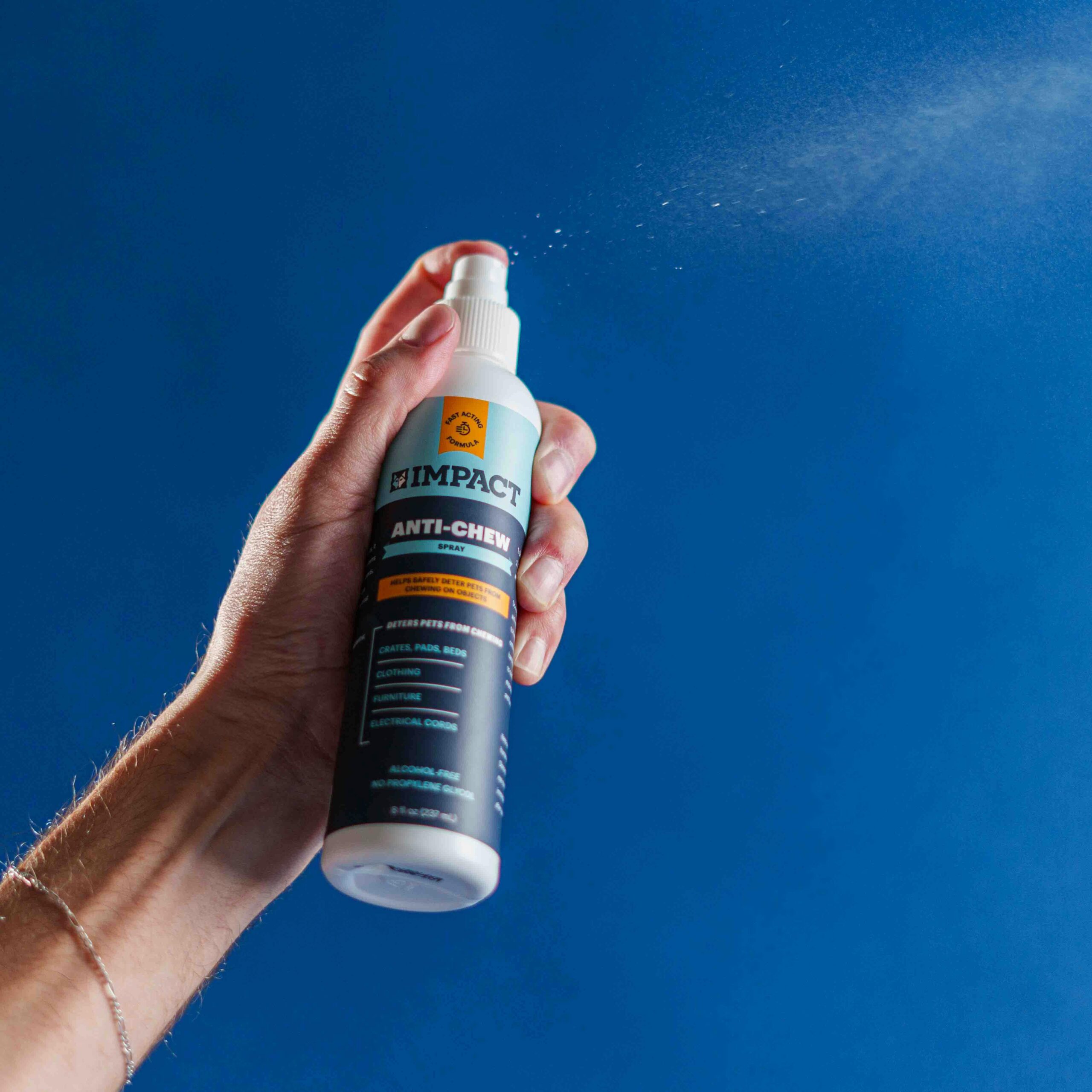 Close-up of hand holding Impact Anti-Chew Spray against blue background.